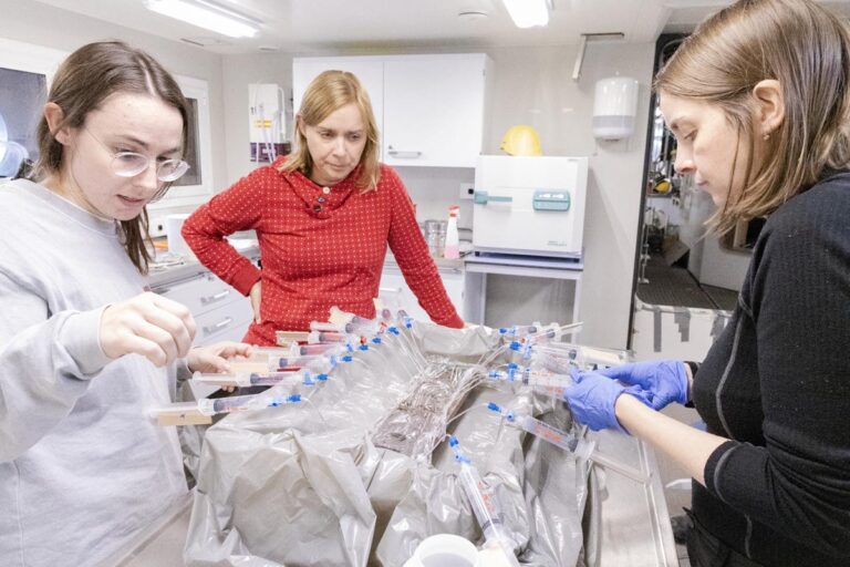 Three people in a lab, affixing syringes to a sediment core.