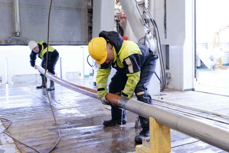 To personer tar en kjerneprøve ut av en gravity corer, i et skips hangar.